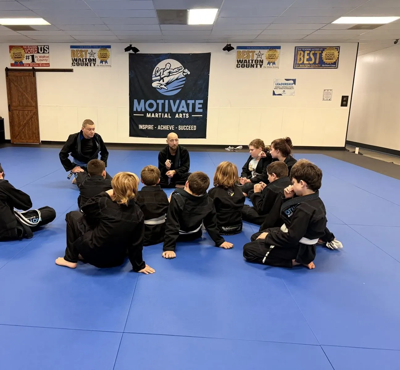 A Juniors BJJ class sitting in a circle with their coaches under the Motivate banner