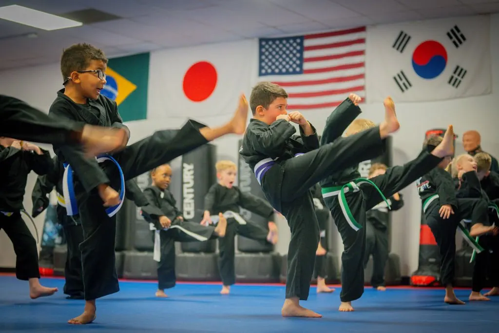 Little Dragons in black uniforms practicing side kicks on the blue mats