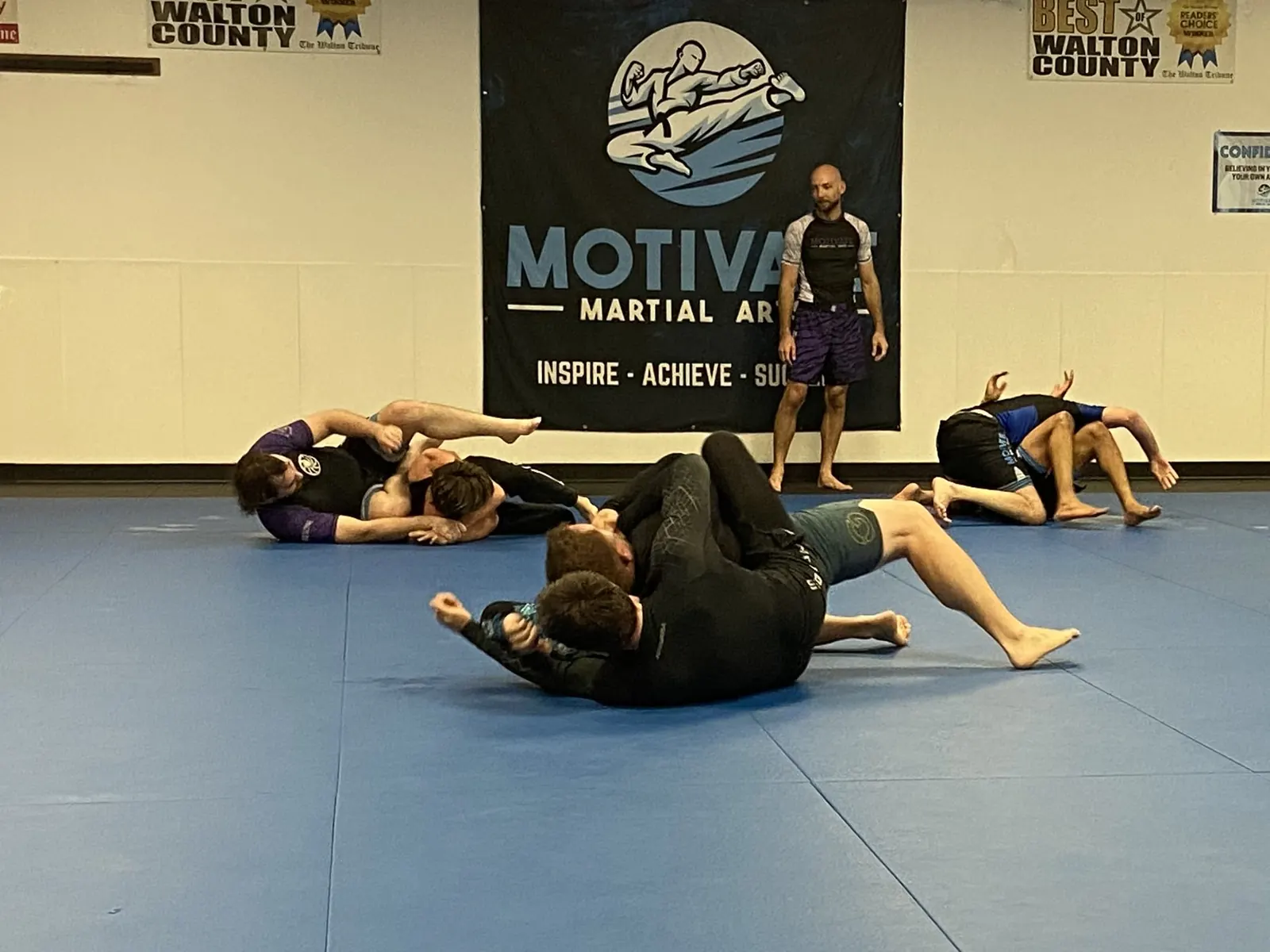 An Adult No-Gi BJJ class drilling in rashguards under the Motivate banner and Best of Walton County awards